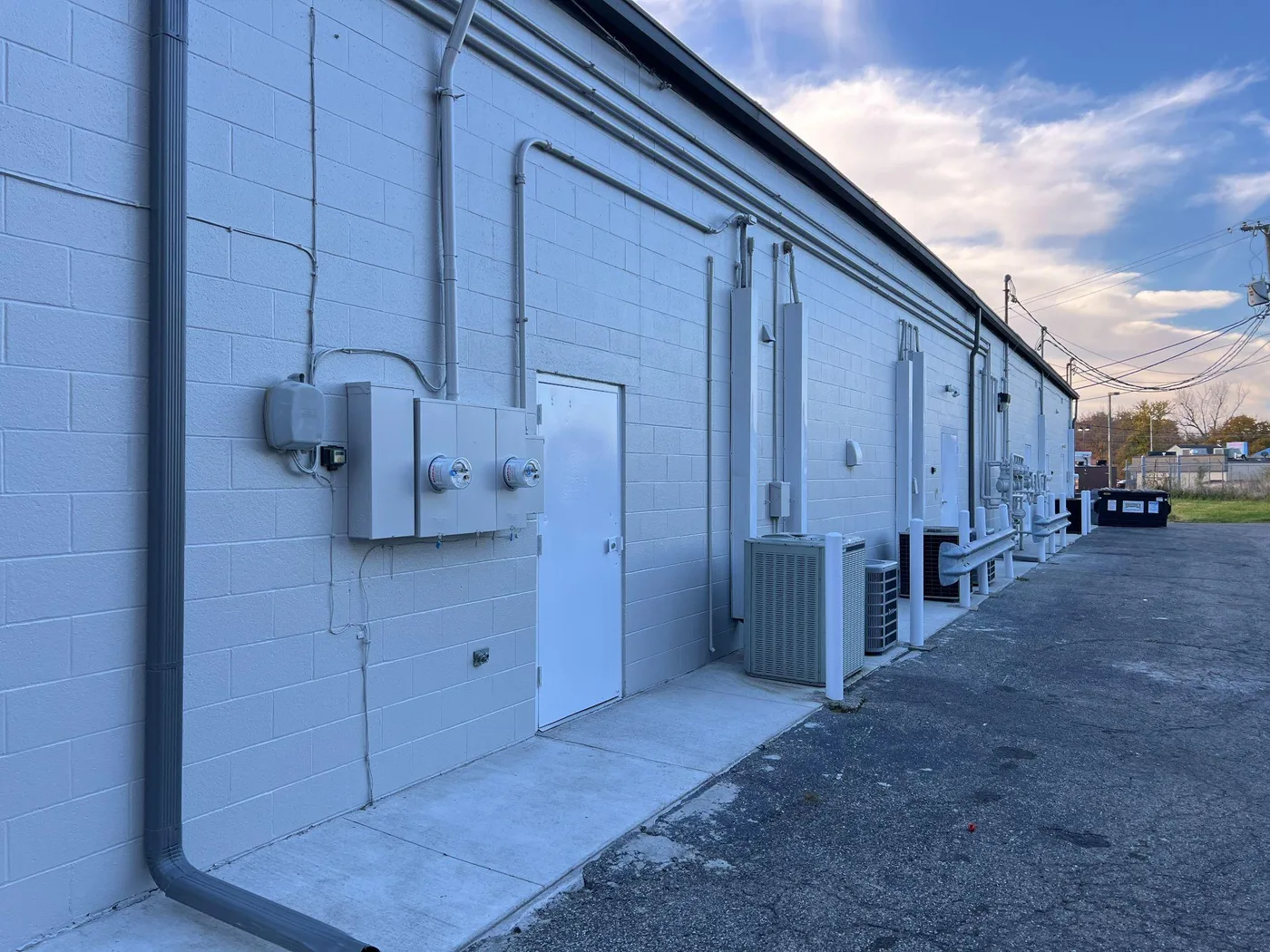 Concrete block commercial building painted light grey with a white service door and roof top units