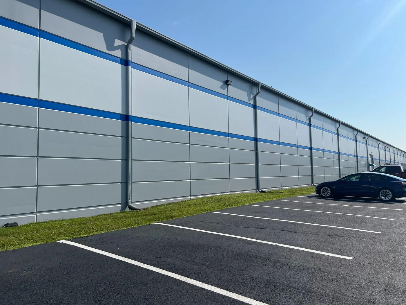 The same grey and blue warehouse wall running back along the edge of the parking lot