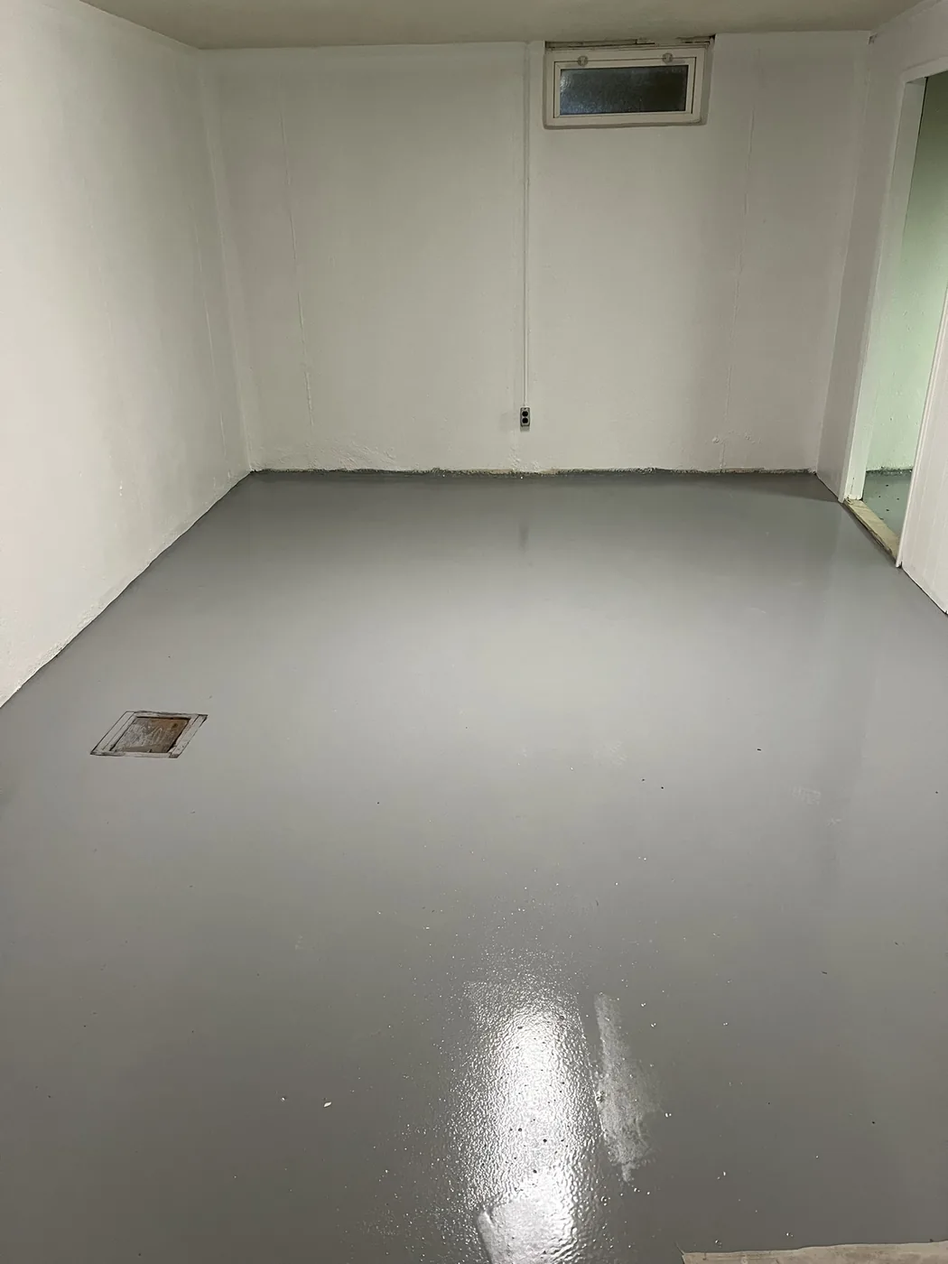 Empty basement room with a smooth grey epoxy floor coating and a floor drain