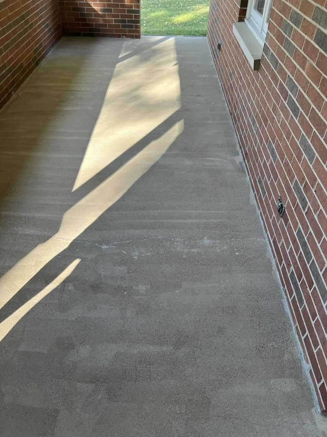 Bare concrete walkway beside a brick home before a flake epoxy coating was applied