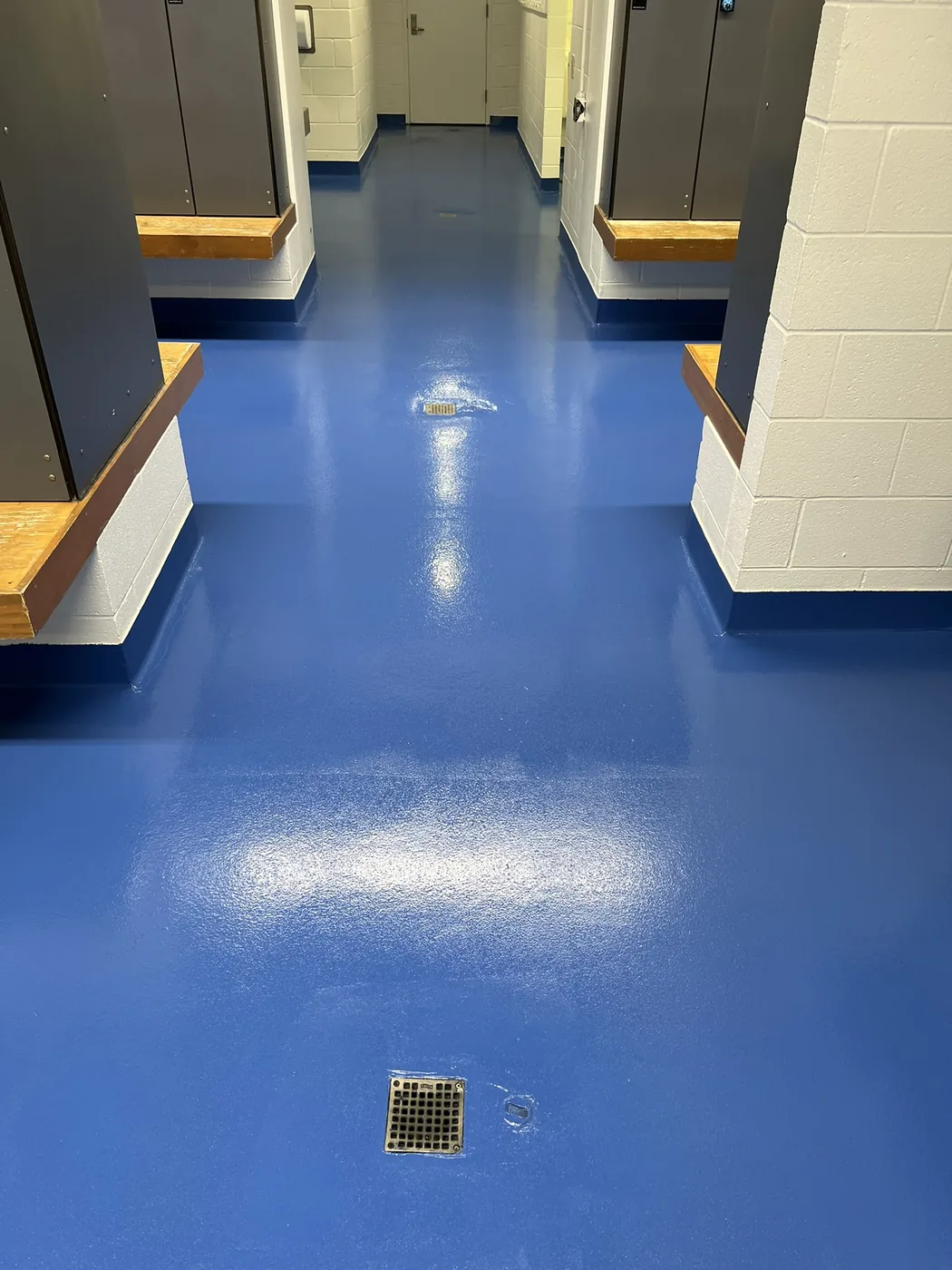 Commercial restroom floor coated in bright blue epoxy with a floor drain