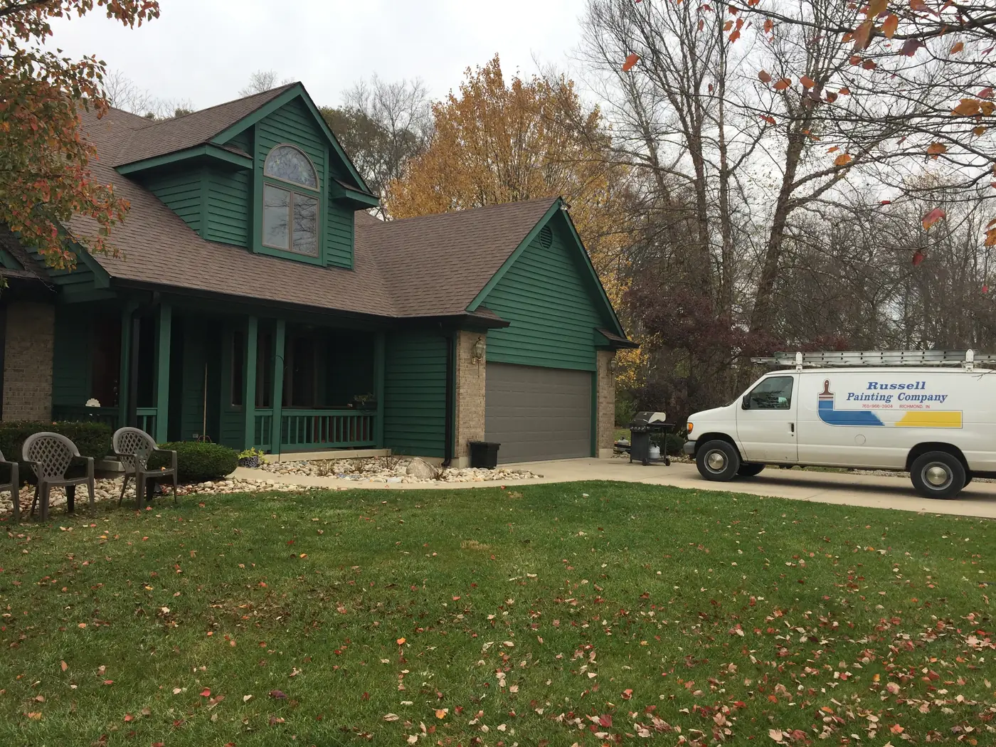 Two story home painted deep green with a Russell Painting Company van parked in the driveway