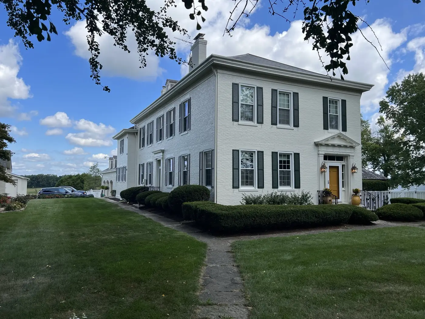 White colonial home with black shutters and trimmed hedges after an exterior painting job