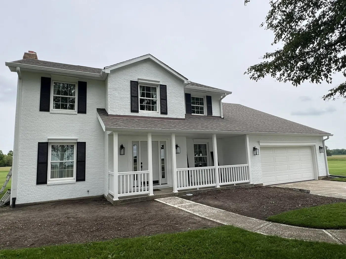 White two story farmhouse with black shutters and a covered front porch after an exterior repaint