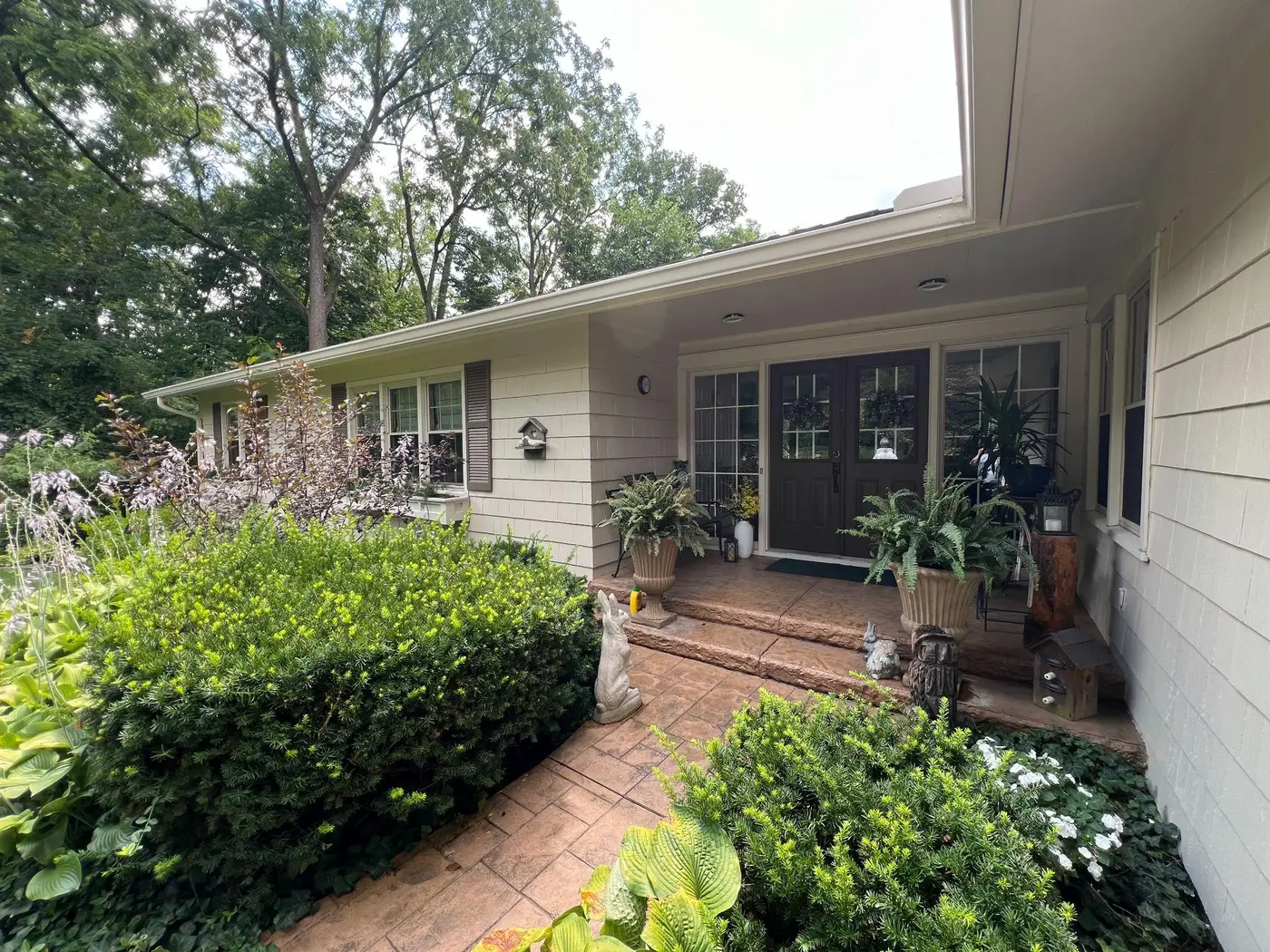 Single story ranch home with light siding, a brick front porch and full landscaping beds