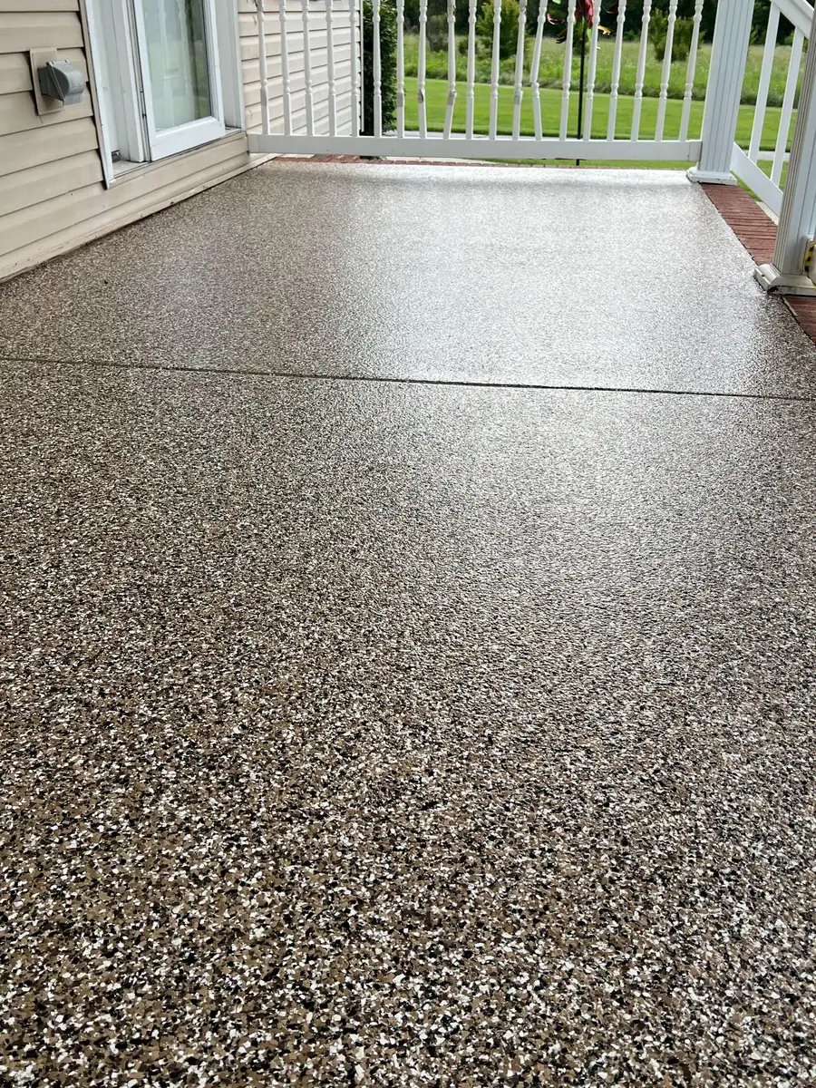 Covered porch finished with a tan flake coating, beside a white railing