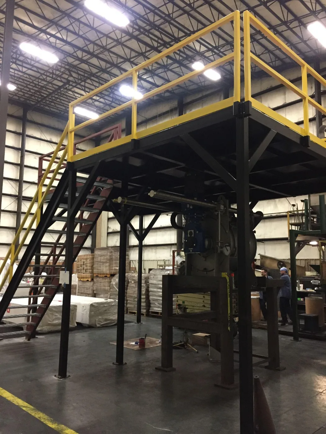 Steel mezzanine platform and stair inside a plant, painted yellow with dark support columns