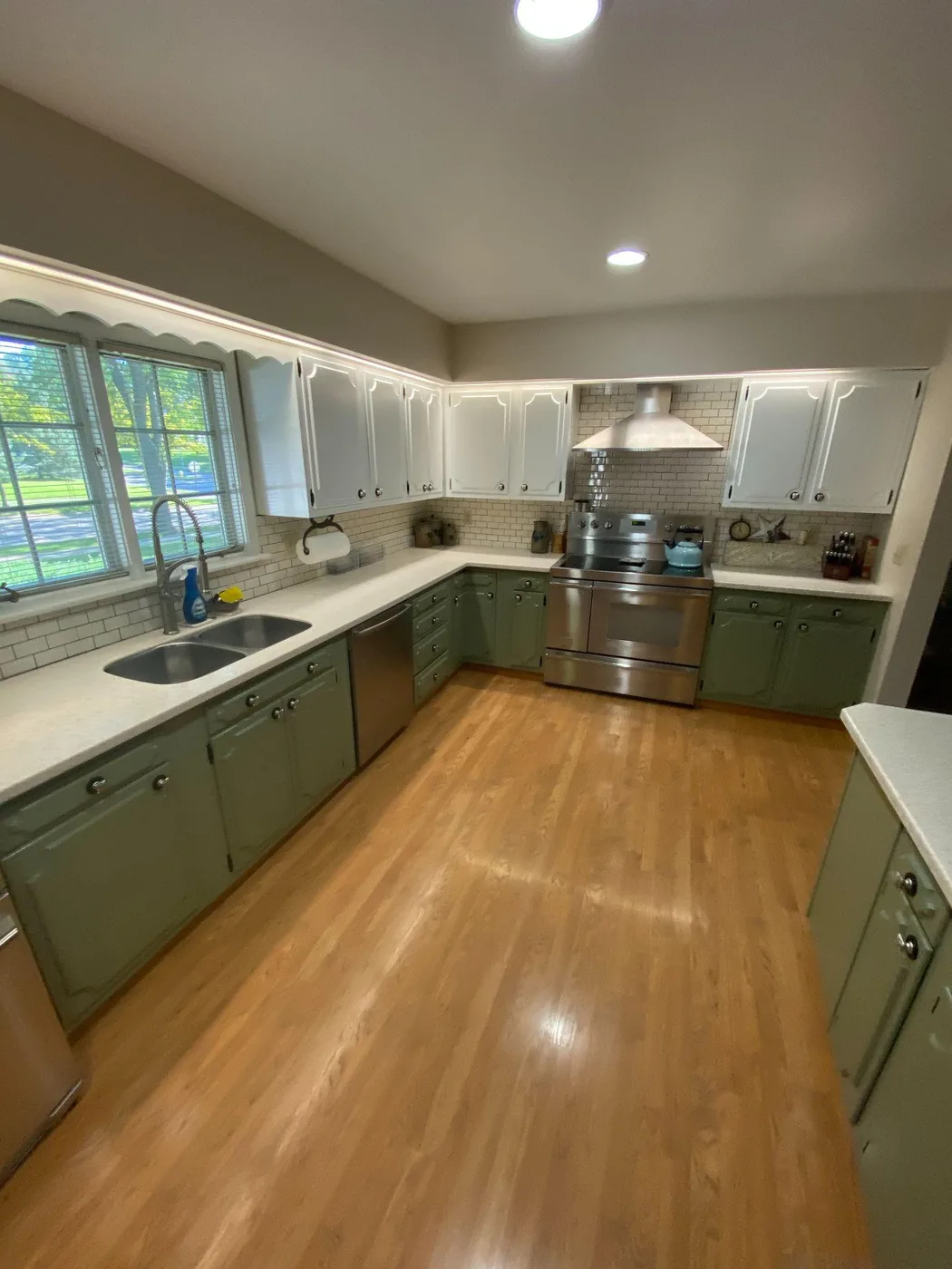 Kitchen with green base cabinets, white wall cabinets and a tile backsplash
